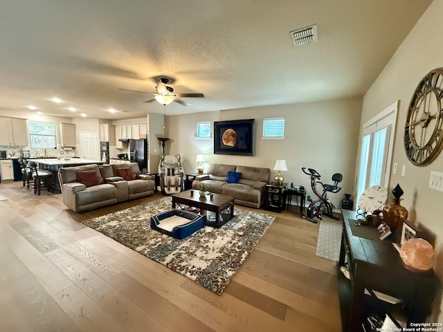 living room with ceiling fan, light hardwood / wood-style floors, and a textured ceiling