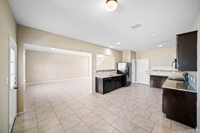 kitchen with backsplash, black fridge, sink, light stone countertops, and light tile patterned floors