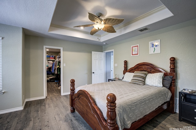 bedroom featuring a raised ceiling, a walk in closet, ceiling fan, and a closet