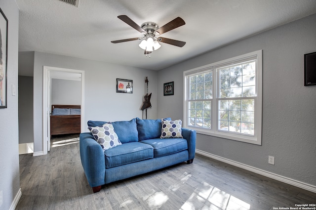 living room featuring ceiling fan, wood-type flooring, and a textured ceiling