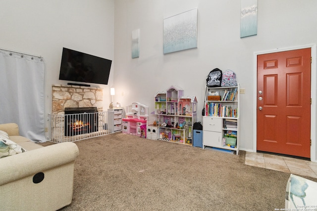 rec room with a stone fireplace, carpet floors, and a high ceiling