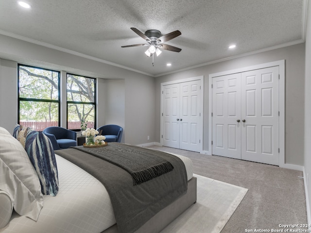 carpeted bedroom with ceiling fan, crown molding, a textured ceiling, and multiple closets