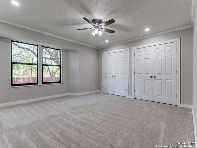 unfurnished bedroom with light carpet, two closets, ceiling fan, ornamental molding, and a textured ceiling