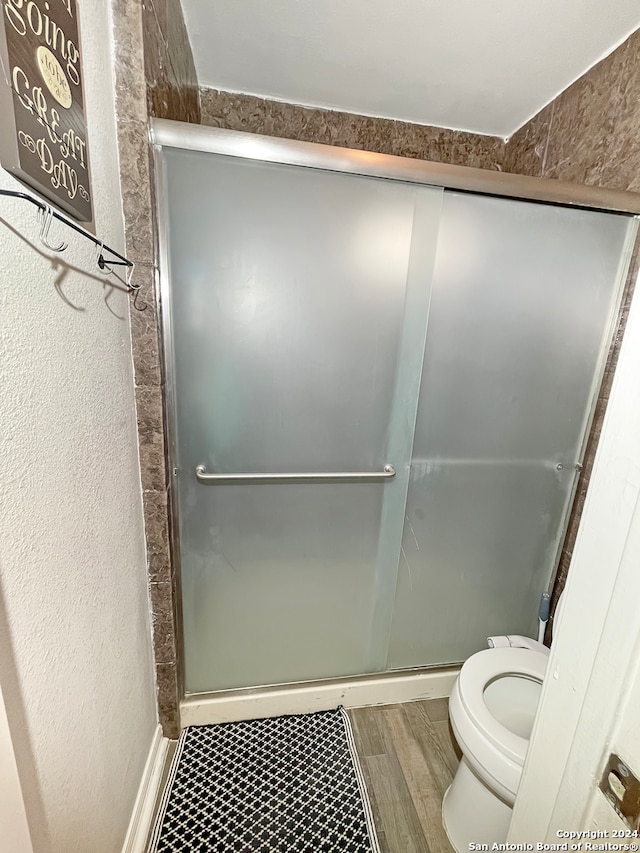 bathroom featuring wood-type flooring, toilet, and a shower with shower door