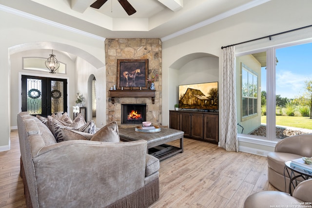 living room featuring a raised ceiling, a stone fireplace, light wood-type flooring, ceiling fan with notable chandelier, and ornamental molding