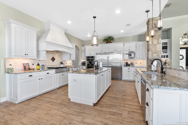 kitchen featuring light wood-type flooring, custom exhaust hood, sink, built in appliances, and hanging light fixtures