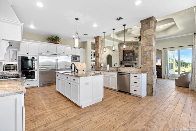 kitchen featuring kitchen peninsula, a raised ceiling, built in appliances, light hardwood / wood-style floors, and hanging light fixtures