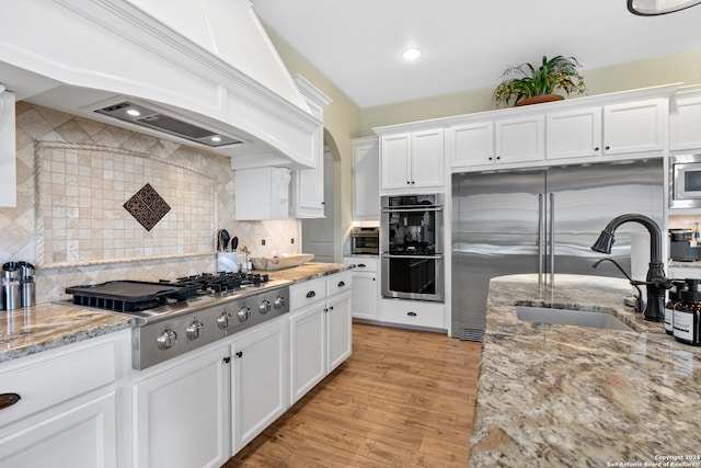 kitchen featuring light hardwood / wood-style flooring, tasteful backsplash, white cabinetry, custom range hood, and stainless steel appliances