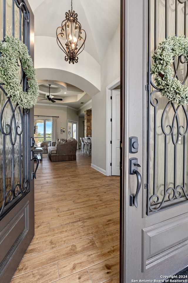 entryway with a raised ceiling, ceiling fan with notable chandelier, light hardwood / wood-style floors, and vaulted ceiling