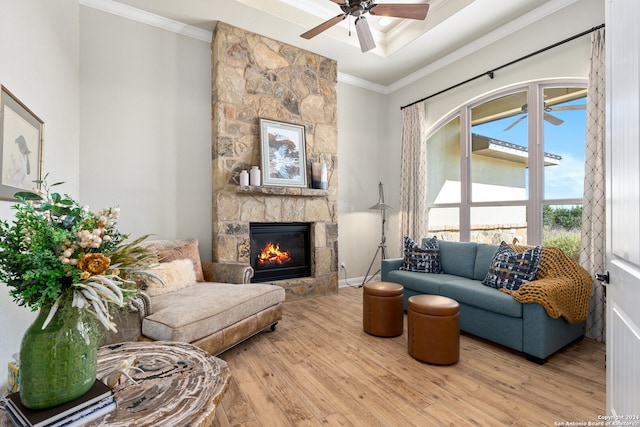 living room featuring ceiling fan, light hardwood / wood-style floors, a stone fireplace, and ornamental molding