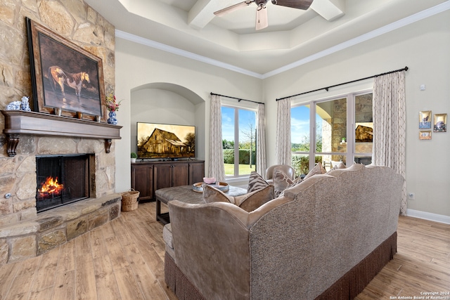 living room featuring a stone fireplace, crown molding, light hardwood / wood-style flooring, and ceiling fan