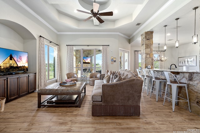 living room featuring ceiling fan with notable chandelier, a raised ceiling, ornamental molding, and light hardwood / wood-style flooring