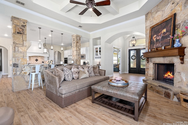 living room featuring a raised ceiling, ceiling fan, crown molding, a fireplace, and light hardwood / wood-style floors