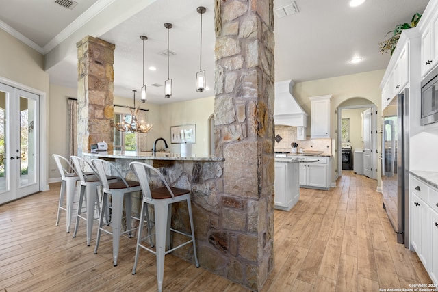 kitchen with premium range hood, white cabinetry, light hardwood / wood-style flooring, and light stone countertops