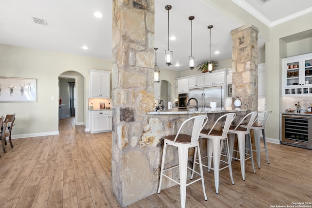 kitchen featuring kitchen peninsula, appliances with stainless steel finishes, light wood-type flooring, light stone counters, and white cabinets