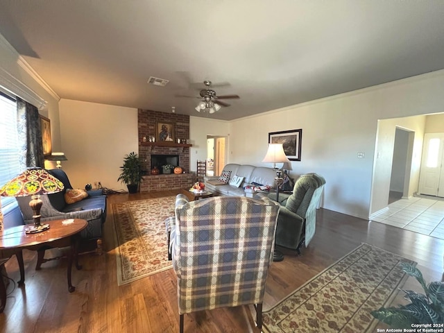 living room featuring hardwood / wood-style flooring, ceiling fan, ornamental molding, and a brick fireplace