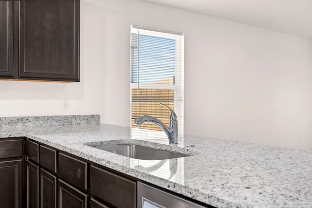 kitchen with dark brown cabinets, light stone counters, and sink