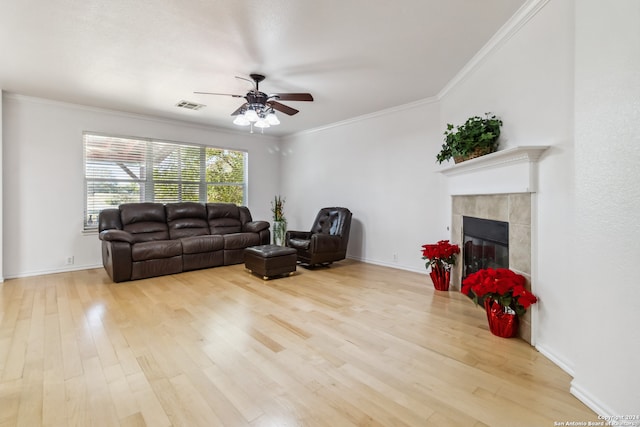 living room with ceiling fan, ornamental molding, a fireplace, and light hardwood / wood-style flooring