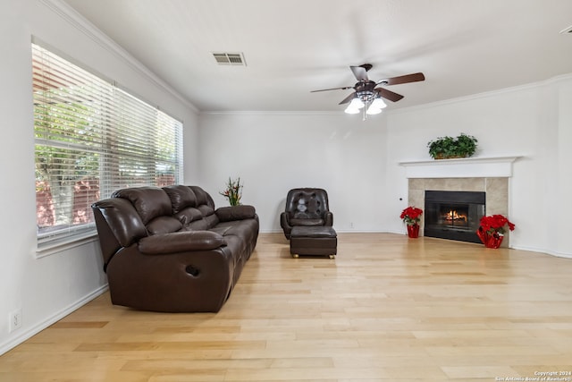 living room featuring light hardwood / wood-style floors, ornamental molding, and a tiled fireplace