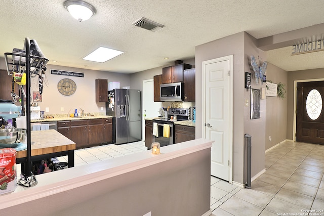 kitchen with sink, light tile patterned floors, stainless steel appliances, and dark brown cabinets