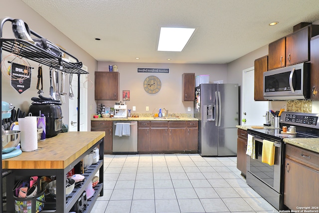 kitchen featuring sink, light tile patterned floors, a textured ceiling, and appliances with stainless steel finishes