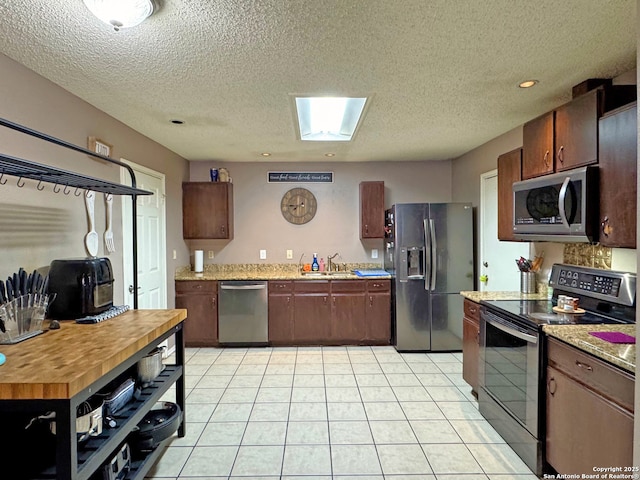9830 Lauren Mist, San Antonio, TX 78251 - kitchen featuring appliances with stainless steel finishes, a sink, a textured ceiling, light tile patterned floors, and a skylight