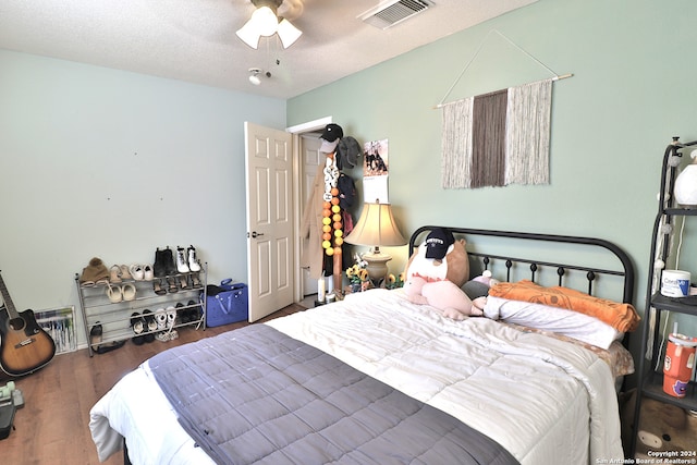 bedroom with a textured ceiling, ceiling fan, and dark hardwood / wood-style floors