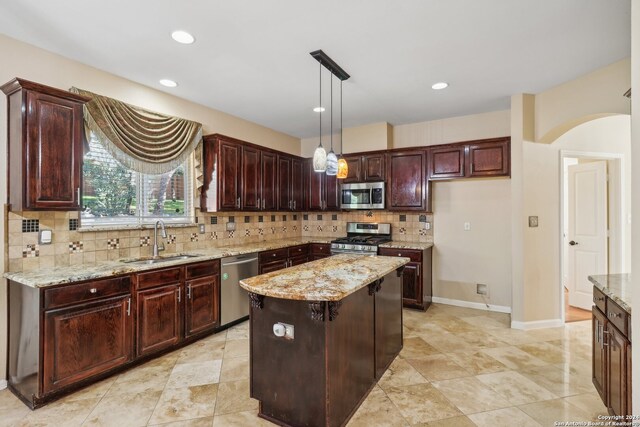 kitchen with backsplash, sink, appliances with stainless steel finishes, decorative light fixtures, and a kitchen island