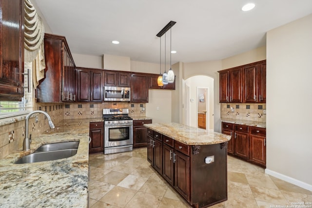 kitchen featuring appliances with stainless steel finishes, tasteful backsplash, light stone counters, sink, and a center island