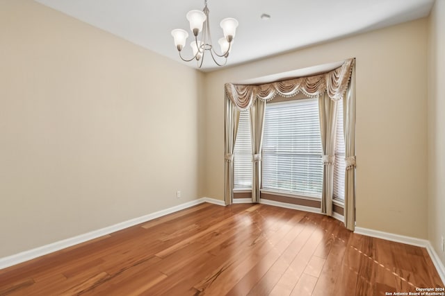 empty room with wood-type flooring and a notable chandelier