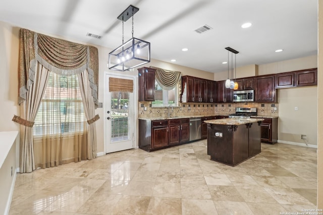 kitchen with light stone countertops, stainless steel appliances, sink, decorative light fixtures, and a center island