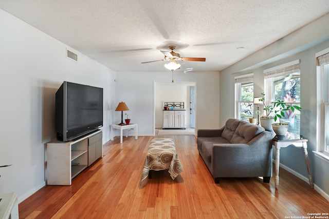 living room featuring a textured ceiling, light wood-type flooring, and ceiling fan