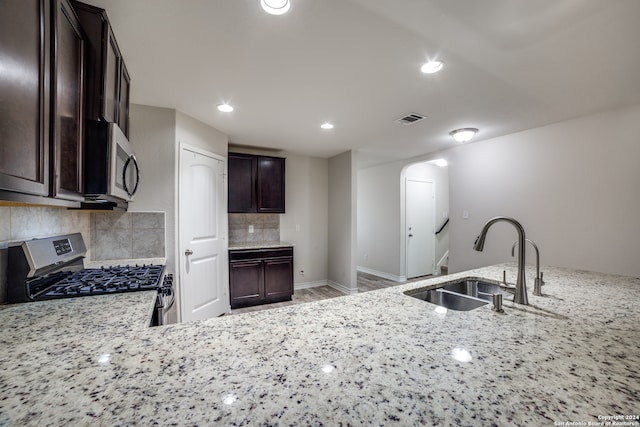 kitchen with backsplash, sink, light stone countertops, dark brown cabinets, and stainless steel appliances