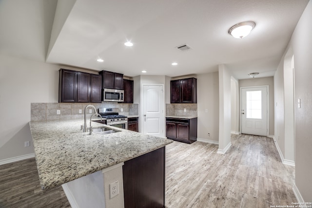 kitchen with backsplash, light hardwood / wood-style flooring, dark brown cabinets, kitchen peninsula, and stainless steel appliances