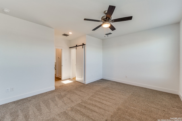 spare room featuring a barn door, carpet floors, and ceiling fan