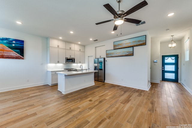 kitchen featuring white cabinets, ceiling fan with notable chandelier, light hardwood / wood-style flooring, appliances with stainless steel finishes, and decorative light fixtures