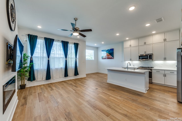 kitchen featuring ceiling fan, white cabinetry, an island with sink, light hardwood / wood-style floors, and appliances with stainless steel finishes