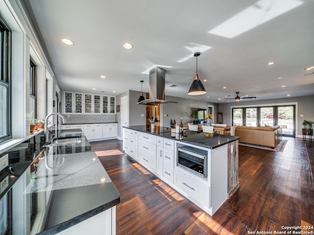 kitchen featuring white cabinetry, sink, dark wood-type flooring, pendant lighting, and island range hood