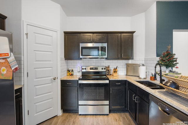 kitchen with light stone countertops, appliances with stainless steel finishes, decorative backsplash, sink, and light hardwood / wood-style flooring