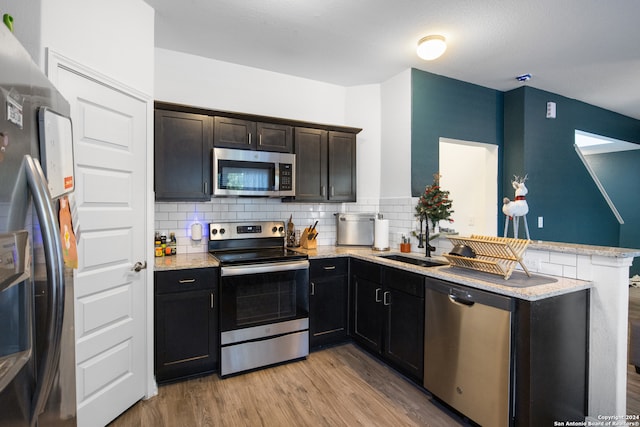 kitchen featuring kitchen peninsula, decorative backsplash, light stone counters, stainless steel appliances, and light hardwood / wood-style flooring