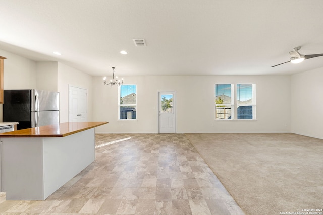 kitchen with wooden counters, stainless steel fridge, pendant lighting, light carpet, and ceiling fan with notable chandelier