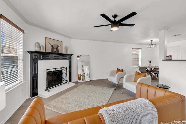 living room featuring light hardwood / wood-style flooring, ornamental molding, ceiling fan with notable chandelier, and a brick fireplace