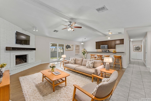 living room with vaulted ceiling with beams, ceiling fan, light hardwood / wood-style flooring, and a brick fireplace