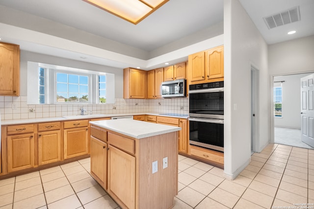 kitchen featuring appliances with stainless steel finishes, tasteful backsplash, sink, light tile patterned floors, and a center island