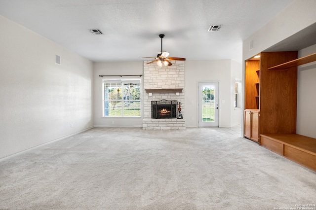 unfurnished living room featuring ceiling fan, a large fireplace, light colored carpet, and a textured ceiling