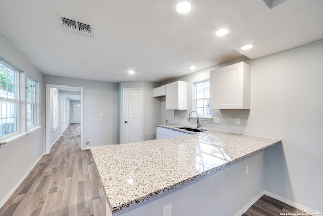 kitchen featuring white cabinets, kitchen peninsula, light stone counters, and sink