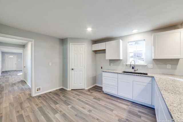 kitchen featuring white cabinets, light stone counters, light hardwood / wood-style flooring, and sink