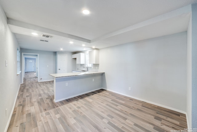 kitchen featuring light hardwood / wood-style floors, white cabinetry, kitchen peninsula, and sink