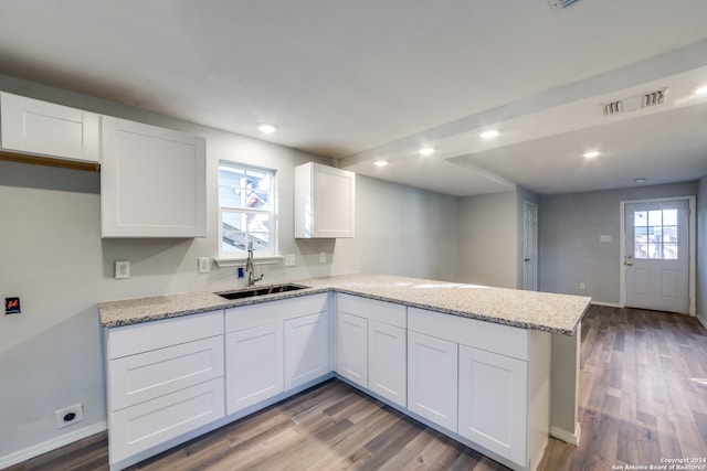 kitchen with kitchen peninsula, light stone countertops, sink, hardwood / wood-style floors, and white cabinetry