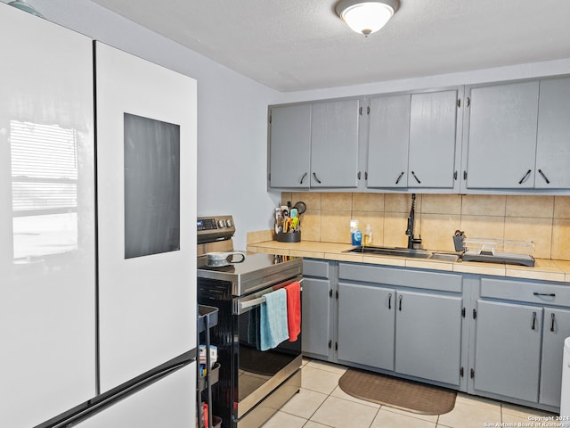 kitchen with gray cabinetry, sink, backsplash, white fridge, and stainless steel electric range